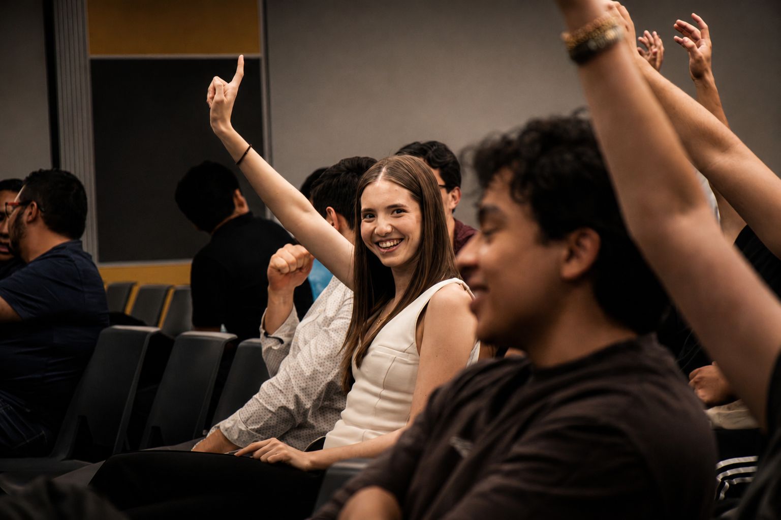 Asistentes levantan la mano y sonríen durante una conferencia